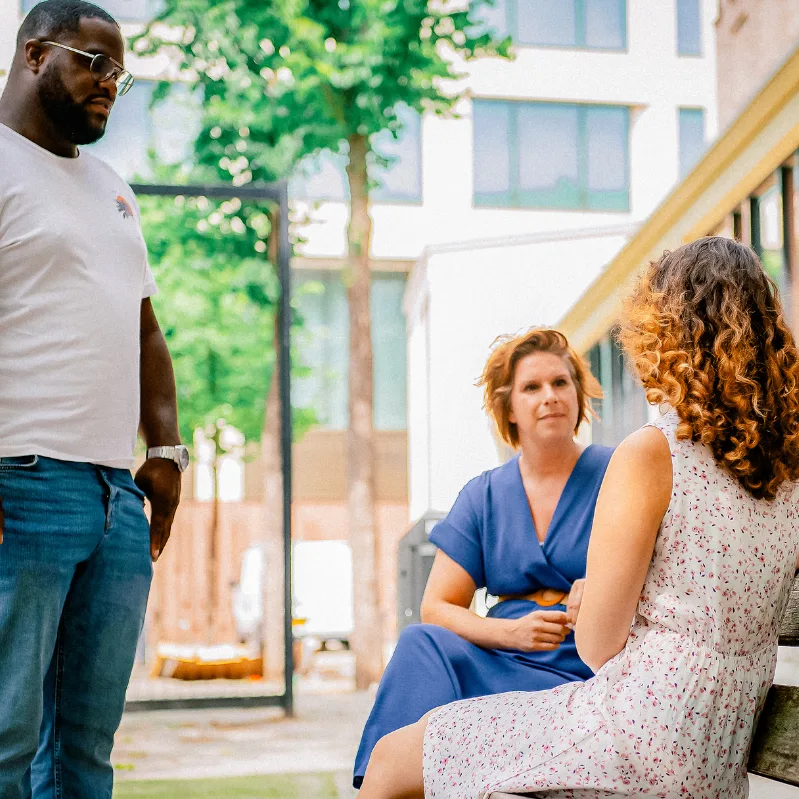 Twee behandelaren spreken een cliënte op een bankje op straat